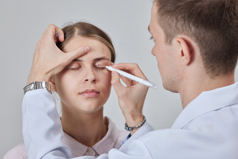 A woman is at a Cosmetic Surgery Affiliates consultation for a blepharoplasty near Fruit Cove and her surgeon is making marks around her eyelids to create a plan for surgery.