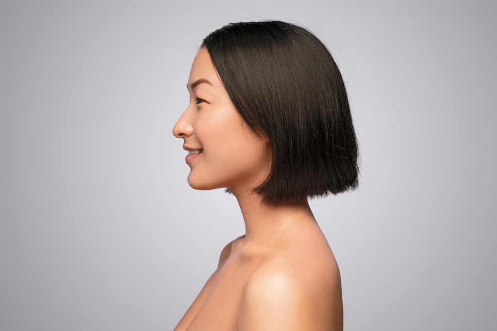 A woman is turned off to the side, smiling, and showing off the results from her double chin removal in OKC.