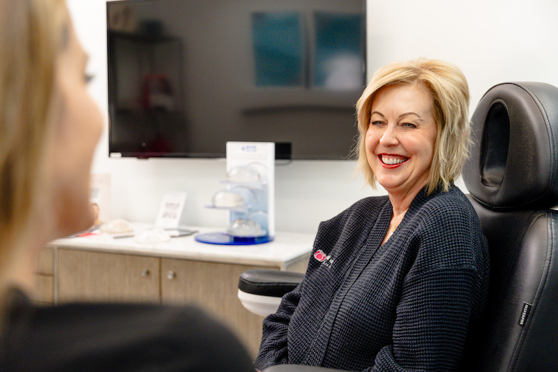 A woman is sitting and smiling as she learns more about excess skin removal in Jacksonville during her initial consultation.